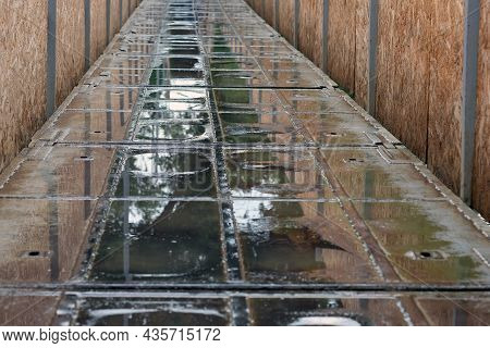 The Road Is Covered With Puddles In The Spring. Metal Bridge Over The River After Rain. Puddles On T