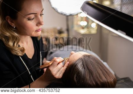Young woman making tatouage for eyebrows in a dressing makeup room. Eyebrows make up process. Make-up artist in beauty studio doing makeup for beautiful girl. Making mua.