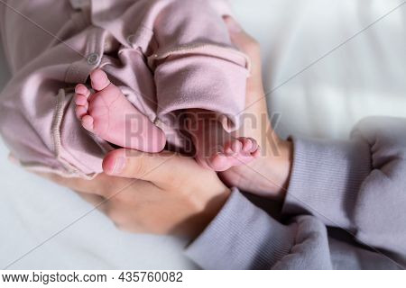 Adorable Newborn Caucasian Baby Girl Legs In Pink Jumpsuit. Little Girls Pink Heels . Top View. Clos