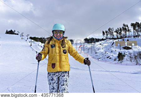 Happy Smiling Young Woman In Yellow Jacket And Ski Helmet Downhill Skiing On A Mountain Slope, Winte