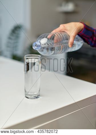 Closeup Of A Ffemale Hand Holding Drinking Water Bottle And Pouring Water Into Glass On Table On Kit