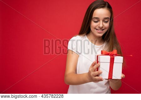 Photo Of Beautiful Positive Happy Little Female Child Isolated Over Red Bacground Wearing Casual Whi