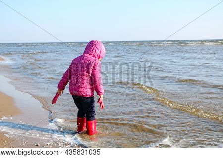 Child Girl Playing By The Sea In Autumn. A Girl In A Red Jacket In A Beautiful Autumn On The Seashor