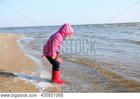 Child Girl Playing By The Sea In Autumn. A Girl In A Red Jacket In A Beautiful Autumn On The Seashor