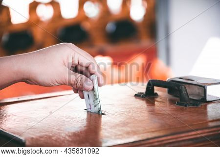 Closeup Of A Hand Holding A Thai Twenty Baht Banknote Being Dropped Into A Donation Wooden Box. Pers