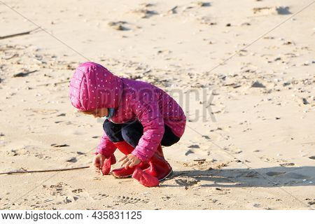 Child Girl Playing By The Sea In Autumn. A Girl In A Red Jacket In A Beautiful Autumn On The Seashor