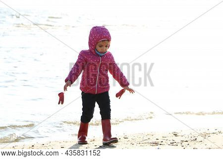 Child Girl Playing By The Sea In Autumn. A Girl In A Red Jacket In A Beautiful Autumn On The Seashor