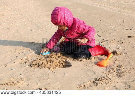 Child Girl Playing By The Sea In Autumn. A Girl In A Red Jacket In A Beautiful Autumn On The Seashor