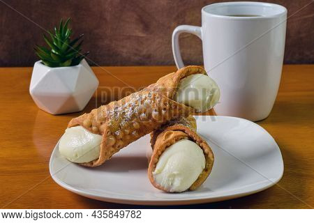 Cream Filled Cannolis Stacked On Top Of Each Other With A Cup Of Coffee