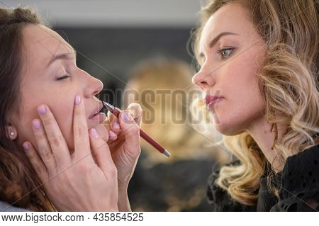 Young woman making makeup in a dressing makeup room. Lips make up process. Make-up artist in beauty studio doing makeup for beautiful girl. Profile - woman making up using pencil for lips. Making mua.