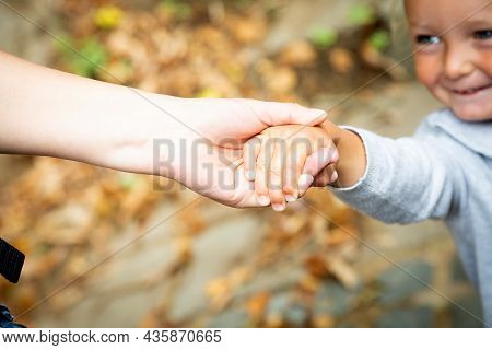 Smiling Caucasian Baby Gives Hand To Mom. Focus On Arms. Autumn Family Walk In Park. Happy Together.