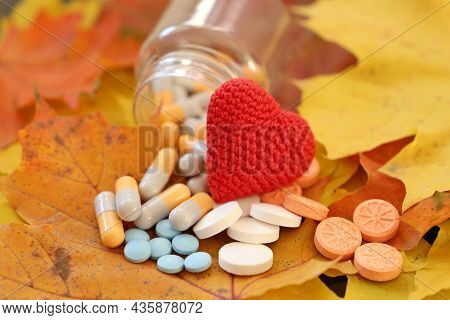 Knitted Red Heart And Pills On Autumn Maple Leaves, Selective Focus. Hypertension, Heart Disease And