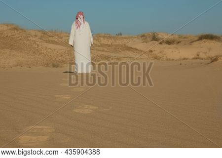 Man In Arabic Clothes Walking Through Desert On Sunny Day, Back View