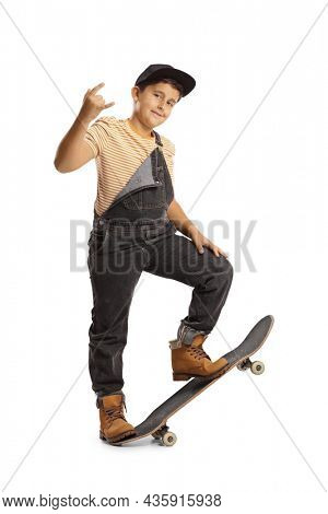 Full length portrait of a boy stepping on a skateboard and gesturing rock and roll sign isolated on white background