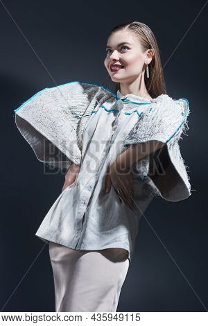 High-fashion shoot. Beautiful girl fashion model poses in extravagant beige blouse with wide sleeves and a beige straight skirt. Studio portrait on a black background.