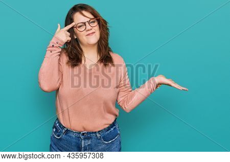 Young plus size woman wearing casual clothes and glasses confused and annoyed with open palm showing copy space and pointing finger to forehead. think about it. 