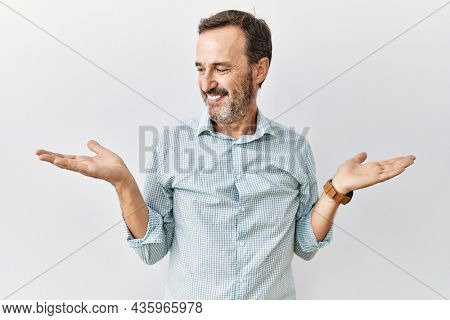 Middle age hispanic man with beard standing over isolated background smiling showing both hands open palms, presenting and advertising comparison and balance 