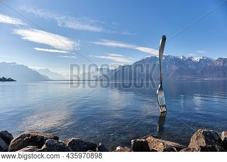 Vevey, Switzerland - Circa 2021: Huge steel fork art installation in Lake Geneva part of the Alimentarium food museum in Vevey, rippling water surface