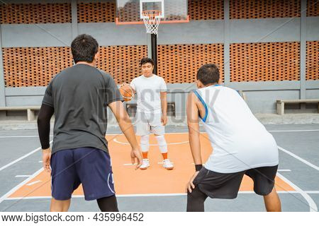 A Male Basketball Player Carrying The Ball Is Blocked By Two Opposing Players In A Ready Position