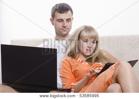 A boy and a girl sitting on the couch with the laptop and tablet