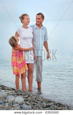 Lykkelig familie med lille pige stående på stranden i aften, ser på mor