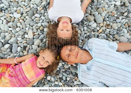 Lykkelig familie med lille pige liggende på stenede strand, med hoveder