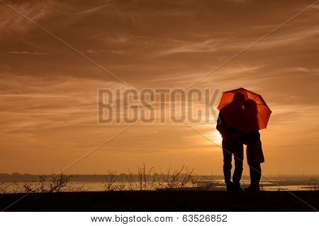 Silhouette Of Pregnant Woman And A Man In The Sunset Under An Umbrela