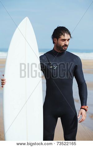 Portrait of handsome surfer man standing with surfboard on the beach
