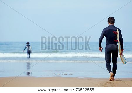 Handsome young surfer man walking at ocean beach holding his surfing board