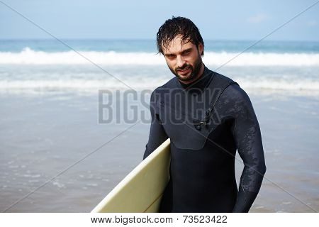 Portrait of handsome surfer man standing with surfboard on the beach