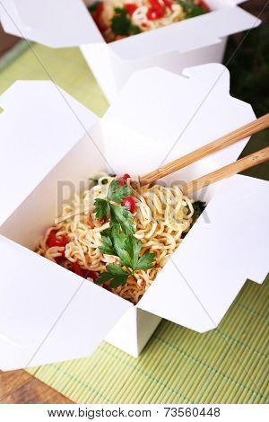 Chinese noodles and sticks in takeaway box on mat background