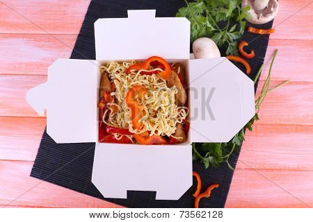 Chinese noodles in takeaway box on black mat on pink background