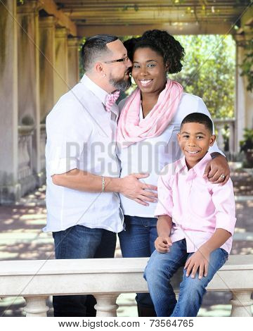 A husband kissing his pregnant wife in a summertime gazebo.  Their son sits oblivious nearby on a balustrade.