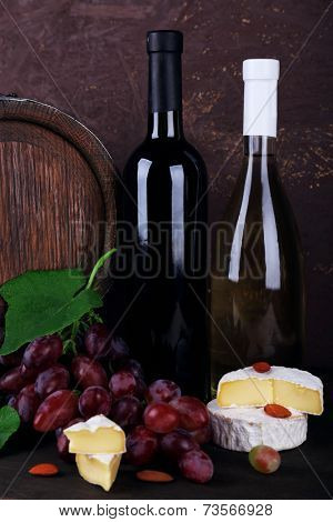 Wine in bottles, Camembert and brie cheese, grapes and wooden barrel on wooden table on wooden background