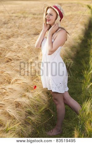 Cheerful Beautiful Young Blonde Girl In White Dress With Straw Hat Posing At Golden Wheat Field