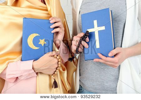Two friends holding books with religions symbols