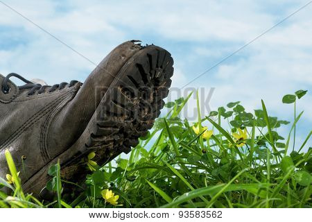 Large boot stepping in grass in extreme closeup symbol for ecological footprint