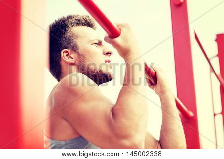 fitness, sport, exercising, training and lifestyle concept - young man doing pull ups on horizontal bar outdoors