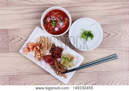 Rice gruel and  side dish  on wood. (Dried shredded pork,Chinese sausage,crispy fish,sausage, fried baby clams,sliced red onion,pickle Chinese cabbage ,Spicy sardine salad and shallots )