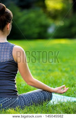 Meditating woman in meditation in city park in yoga pose. Girl relaxing with serene relaxed expression outside in summer. Beautiful young Caucasian female model. Close up