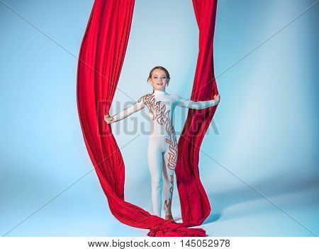 Graceful gymnast performing aerial exercise with red fabrics on blue background