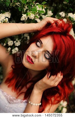 Beautiful girl (25 years old) in white wedding dress on a background of spirea bushes with lots of small white flowers