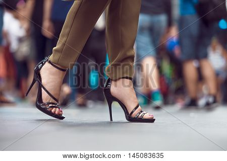 Woman wearing black high heels summer shoes walkin in the city crowd. Woman feet making step on city street. Female legs and feet with shoes close-up.