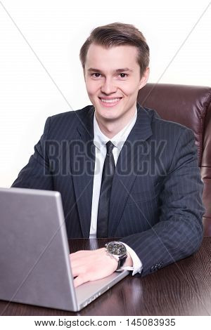Young happy businessman sitting in the office and working on laptop smilng. Young student man got new ofice job after university.