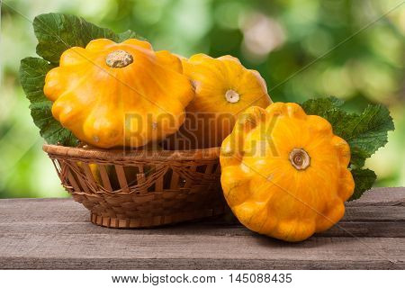 yellow pattypan squash with leaf in a wicker basket on a wooden table with a blurred background.