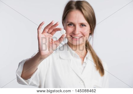 Doctor woman showing pill. Young female medical professional isolated on white background. Selective focus