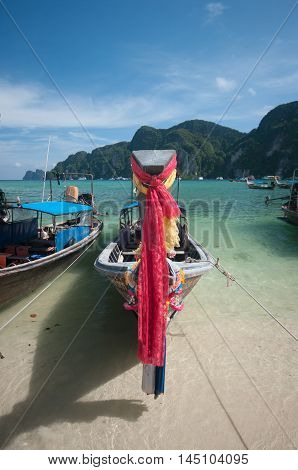 Colourful prayer scarves hang from bows of longtail taxi boats anchored at beach Ao Nang Thailand
