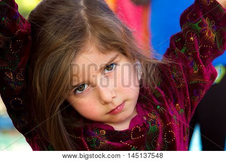 An irritated little girl gives an intense look. She has her arms up and is leaning on something with her head cocked to the side looking at the viewer with a furrowed brow and intense eyes.