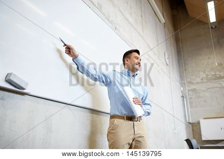 education, school, business, teaching and people concept - happy teacher or businessman pointing marker to white board at lecture