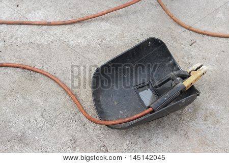welding mask still life of rod-holder with cable and electrode for electric arc  on a cement floor.
